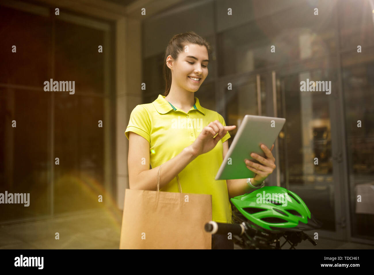 Giovane donna in maglia gialla erogazione di pacchetto utilizzando i gadget per via ordine presso la città della strada. Corriere on-line utilizzando app per ricevere il pagamento e il tracking spedizioni indirizzo. Le moderne tecnologie. Foto Stock