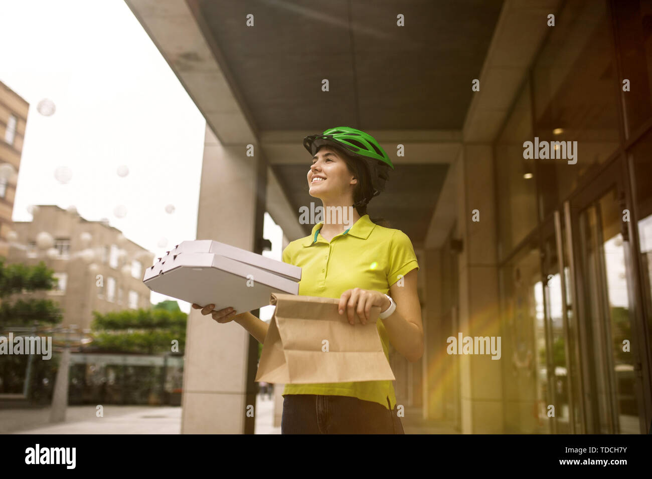 Giovane donna in maglia gialla consegna pizza con i gadget per via ordine presso la città della strada. Corriere on-line utilizzando app per ricevere il pagamento e il tracking spedizioni indirizzo. Le moderne tecnologie. Foto Stock