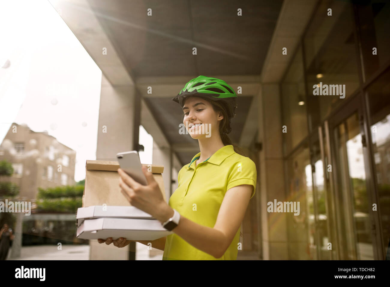 Giovane donna in maglia gialla consegna pizza con i gadget per via ordine presso la città della strada. Corriere on-line utilizzando app per ricevere il pagamento e il tracking spedizioni indirizzo. Le moderne tecnologie. Foto Stock
