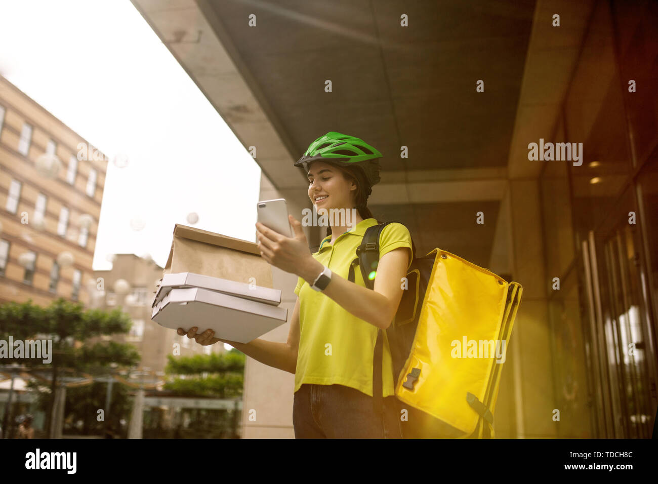 Giovane donna in maglia gialla consegna pizza con i gadget per via ordine presso la città della strada. Corriere on-line utilizzando app per ricevere il pagamento e il tracking spedizioni indirizzo. Le moderne tecnologie. Foto Stock