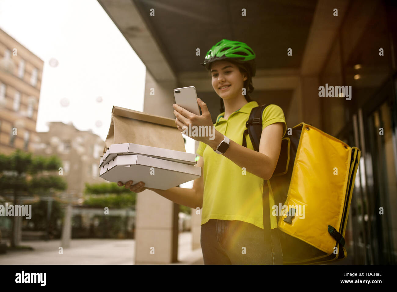 Giovane donna in maglia gialla consegna pizza con i gadget per via ordine presso la città della strada. Corriere on-line utilizzando app per ricevere il pagamento e il tracking spedizioni indirizzo. Le moderne tecnologie. Foto Stock