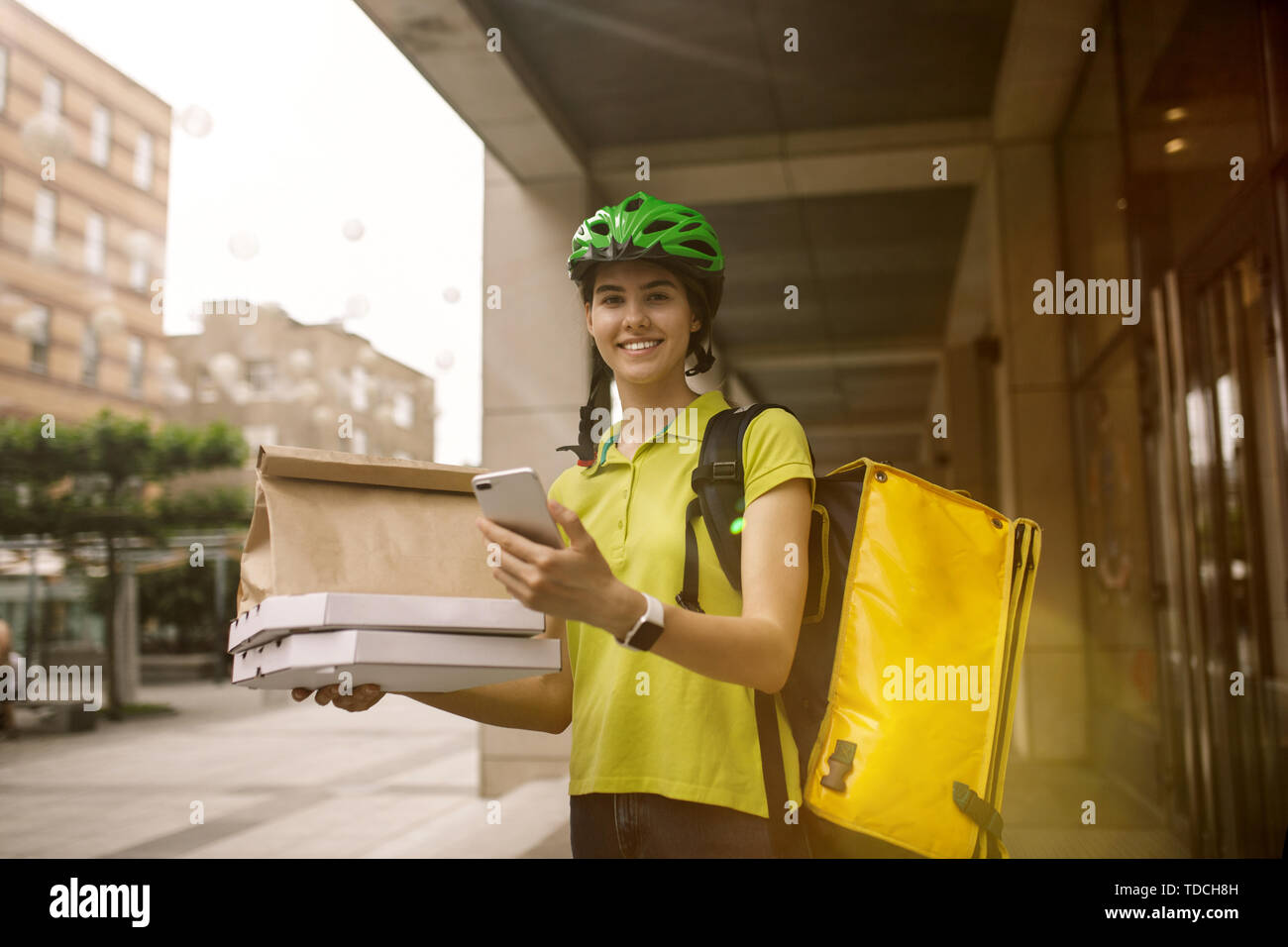 Giovane donna in maglia gialla consegna pizza con i gadget per via ordine presso la città della strada. Corriere on-line utilizzando app per ricevere il pagamento e il tracking spedizioni indirizzo. Le moderne tecnologie. Foto Stock