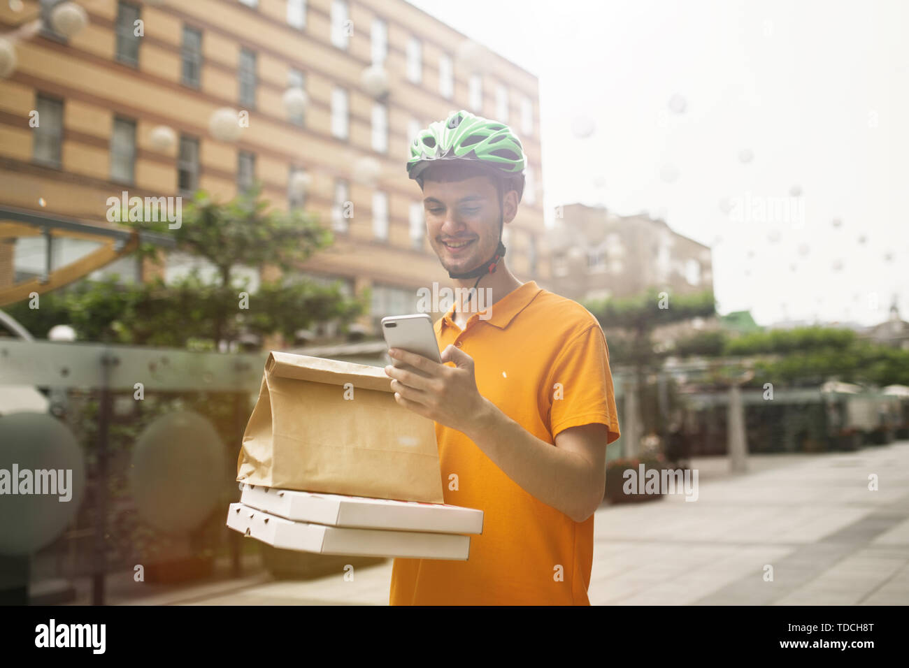 Giovane uomo in maglietta gialla consegna pizza con i gadget per via ordine presso la città della strada. Corriere on-line utilizzando app per ricevere il pagamento e il tracking spedizioni indirizzo. Le moderne tecnologie. Foto Stock