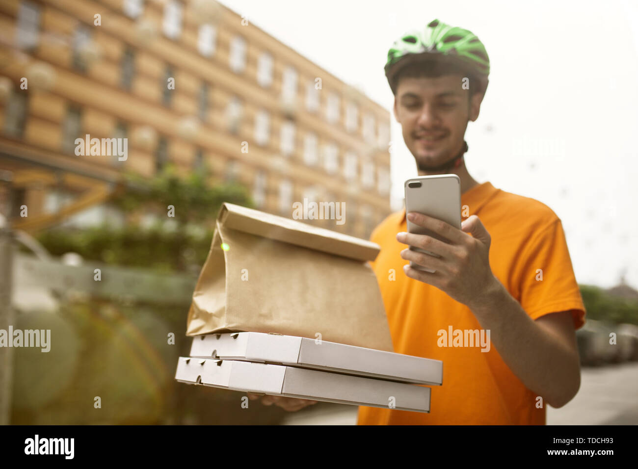 Giovane uomo in maglietta gialla consegna pizza con i gadget per via ordine presso la città della strada. Corriere on-line utilizzando app per ricevere il pagamento e il tracking spedizioni indirizzo. Le moderne tecnologie. Foto Stock