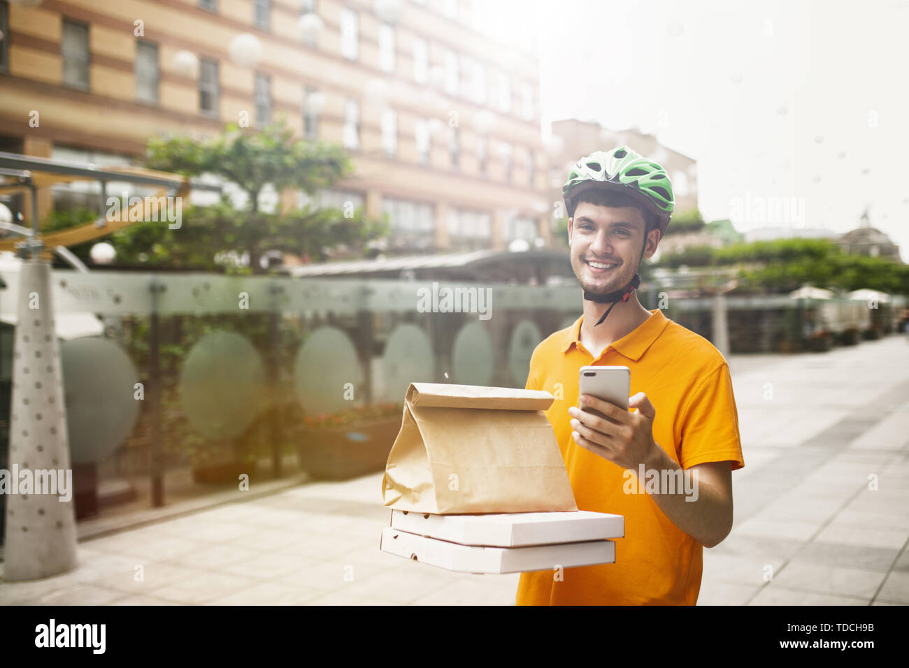 Giovane uomo in maglietta gialla consegna pizza con i gadget per via ordine presso la città della strada. Corriere on-line utilizzando app per ricevere il pagamento e il tracking spedizioni indirizzo. Le moderne tecnologie. Foto Stock