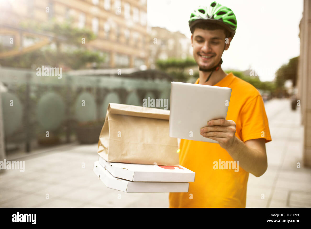 Giovane uomo in maglietta gialla consegna pizza con i gadget per via ordine presso la città della strada. Corriere on-line utilizzando app per ricevere il pagamento e il tracking spedizioni indirizzo. Le moderne tecnologie. Foto Stock