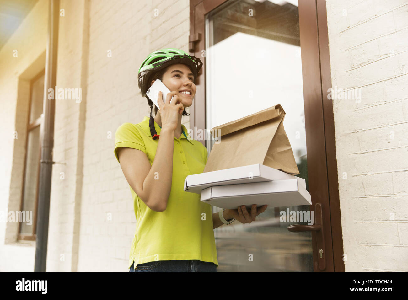 Giovane donna in maglia gialla consegna pizza con i gadget per via ordine presso la città della strada. Corriere on-line utilizzando app per ricevere il pagamento e il tracking spedizioni indirizzo. Le moderne tecnologie. Foto Stock