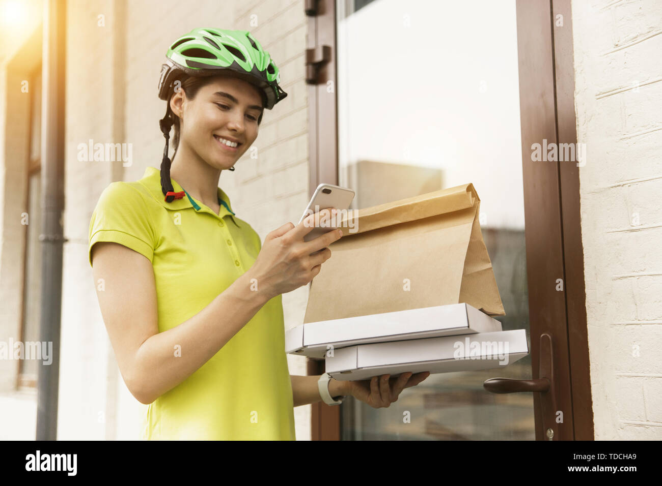 Giovane donna in maglia gialla consegna pizza con i gadget per via ordine presso la città della strada. Corriere on-line utilizzando app per ricevere il pagamento e il tracking spedizioni indirizzo. Le moderne tecnologie. Foto Stock