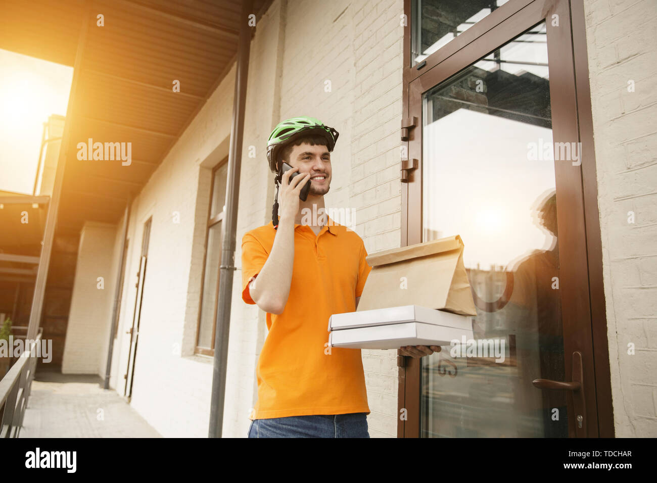 Giovane uomo in maglietta gialla consegna pizza con i gadget per via ordine presso la città della strada. Corriere on-line utilizzando app per ricevere il pagamento e il tracking spedizioni indirizzo. Le moderne tecnologie. Foto Stock