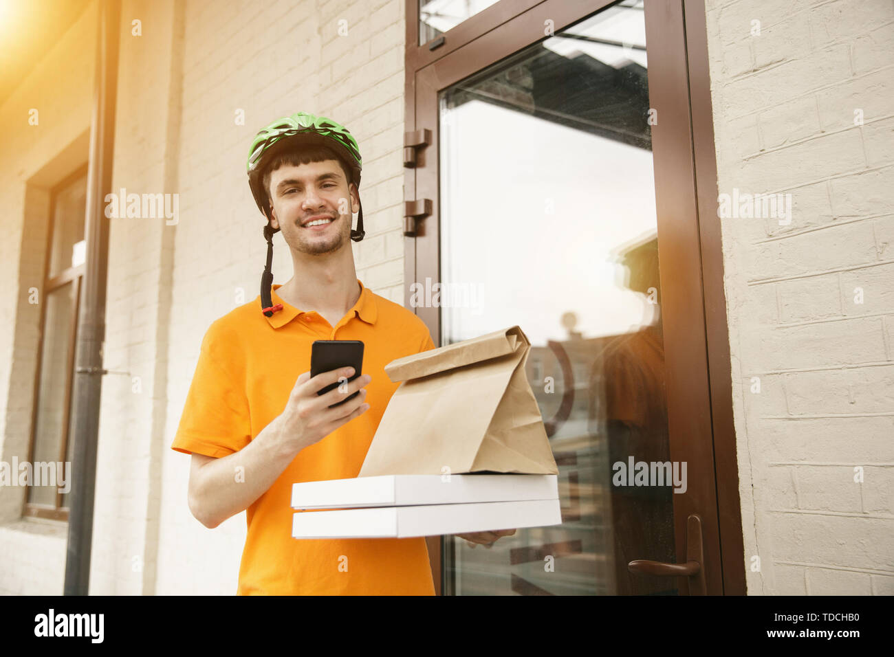 Giovane uomo in maglietta gialla consegna pizza con i gadget per via ordine presso la città della strada. Corriere on-line utilizzando app per ricevere il pagamento e il tracking spedizioni indirizzo. Le moderne tecnologie. Foto Stock