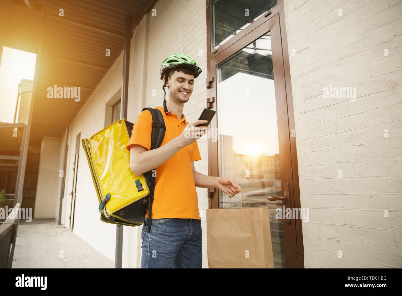 Giovane uomo in maglietta gialla consegna pizza con i gadget per via ordine presso la città della strada. Corriere on-line utilizzando app per ricevere il pagamento e il tracking spedizioni indirizzo. Le moderne tecnologie. Foto Stock