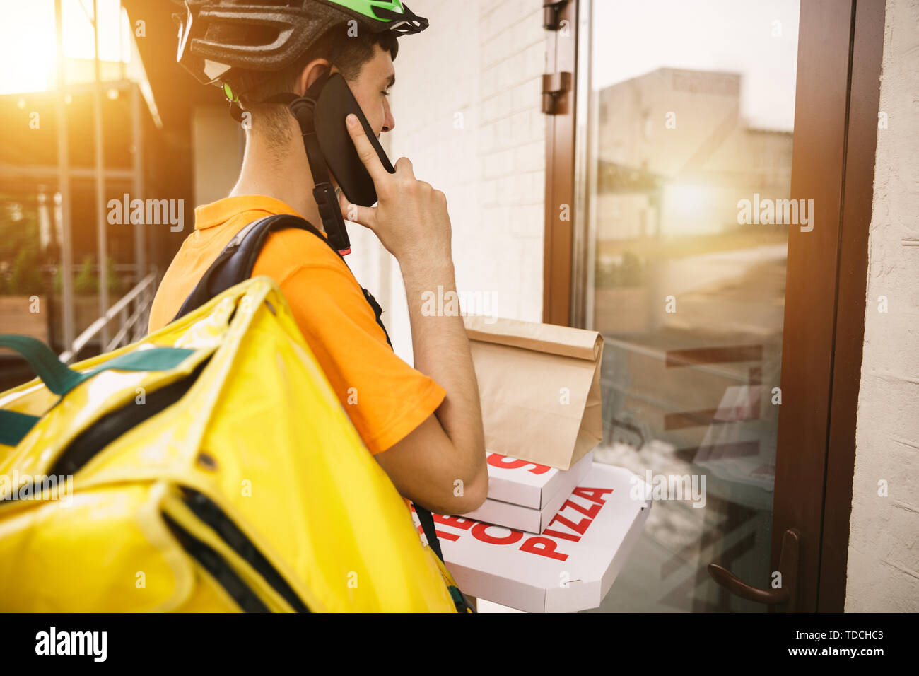 Giovane uomo in maglietta gialla consegna pizza con i gadget per via ordine presso la città della strada. Corriere on-line utilizzando app per ricevere il pagamento e il tracking spedizioni indirizzo. Le moderne tecnologie. Foto Stock