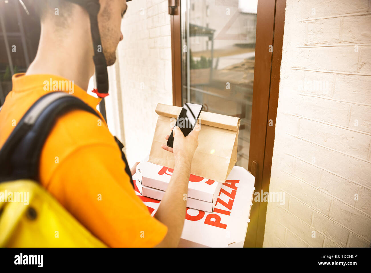 Giovane uomo in maglietta gialla consegna pizza con i gadget per via ordine presso la città della strada. Corriere on-line utilizzando app per ricevere il pagamento e il tracking spedizioni indirizzo. Le moderne tecnologie. Foto Stock