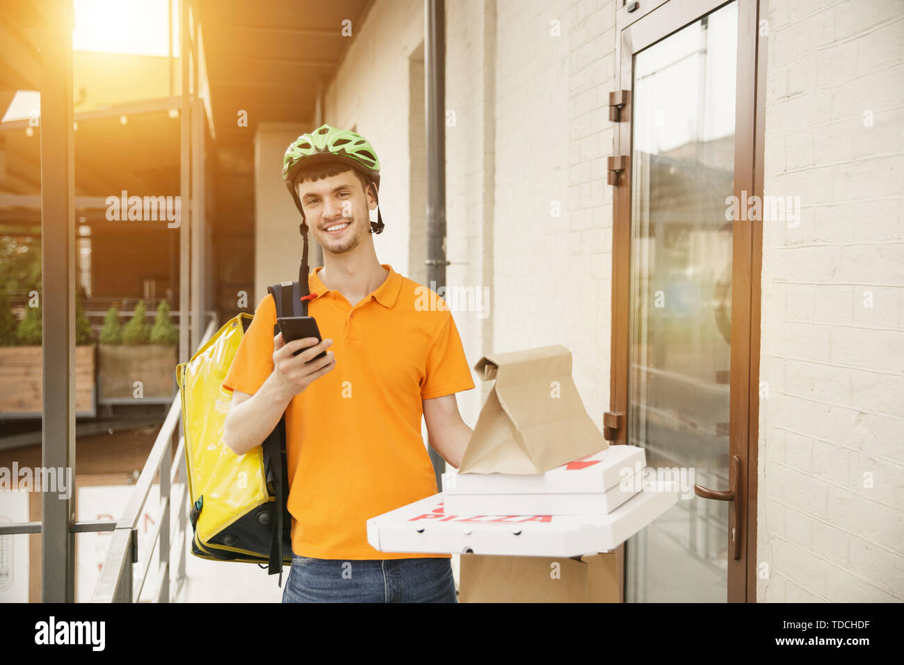 Giovane uomo in maglietta gialla consegna pizza con i gadget per via ordine presso la città della strada. Corriere on-line utilizzando app per ricevere il pagamento e il tracking spedizioni indirizzo. Le moderne tecnologie. Foto Stock
