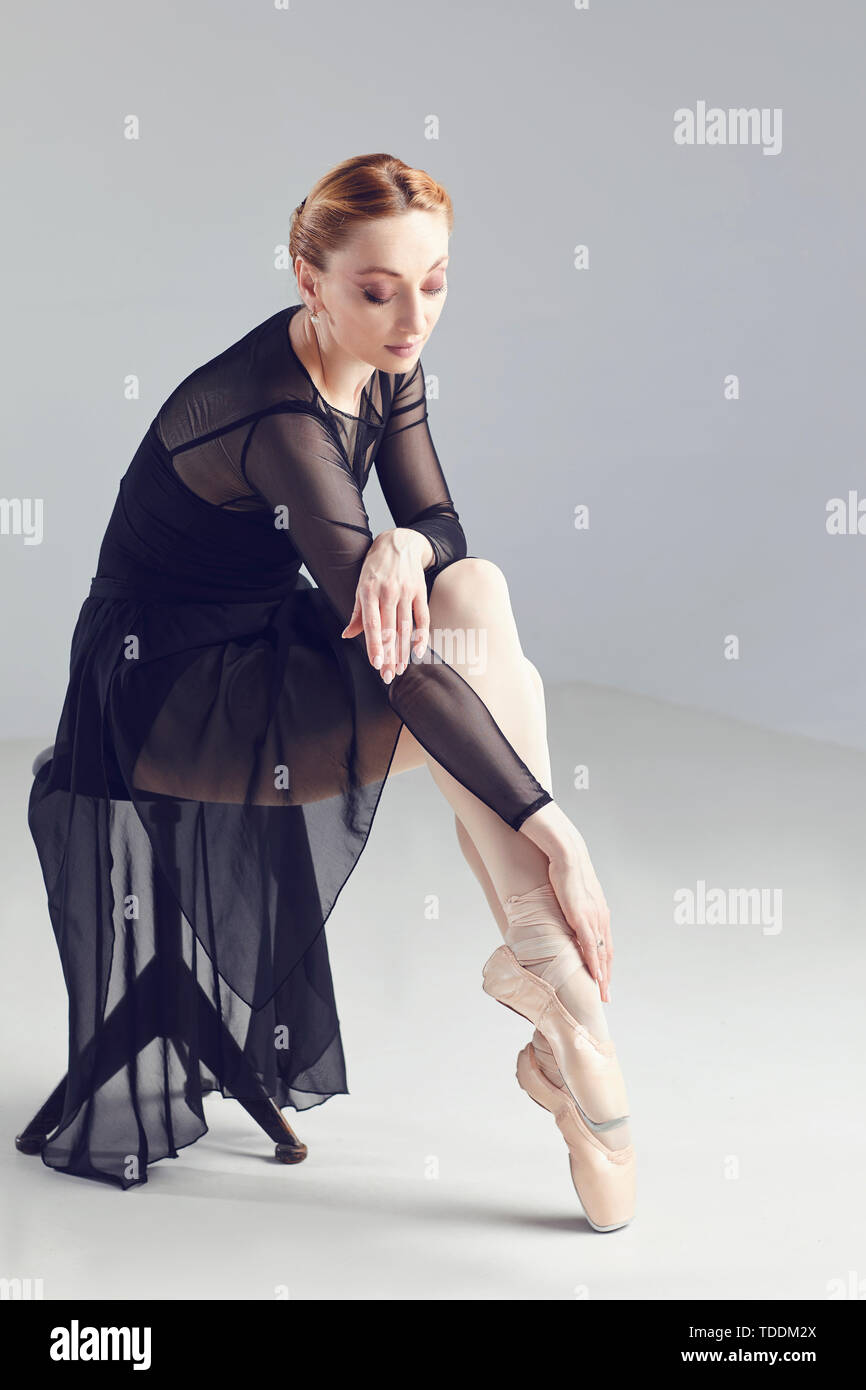 La ballerina donna in abito nero in posa seduta su una sedia Foto Stock