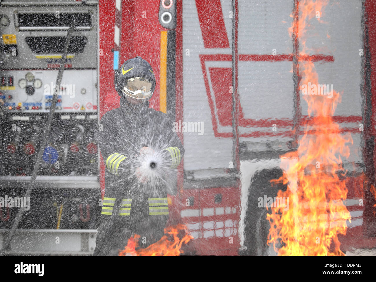 Vigile del fuoco con il casco e uniforme in azione e fiamme di fuoco Foto Stock