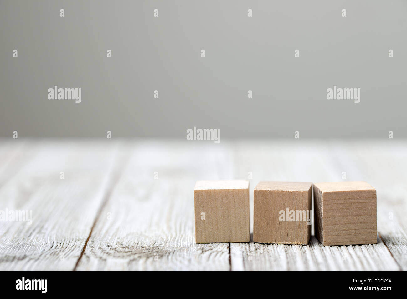 Tre giocattolo di legno i cubi su grigio Sfondo di legno Foto Stock