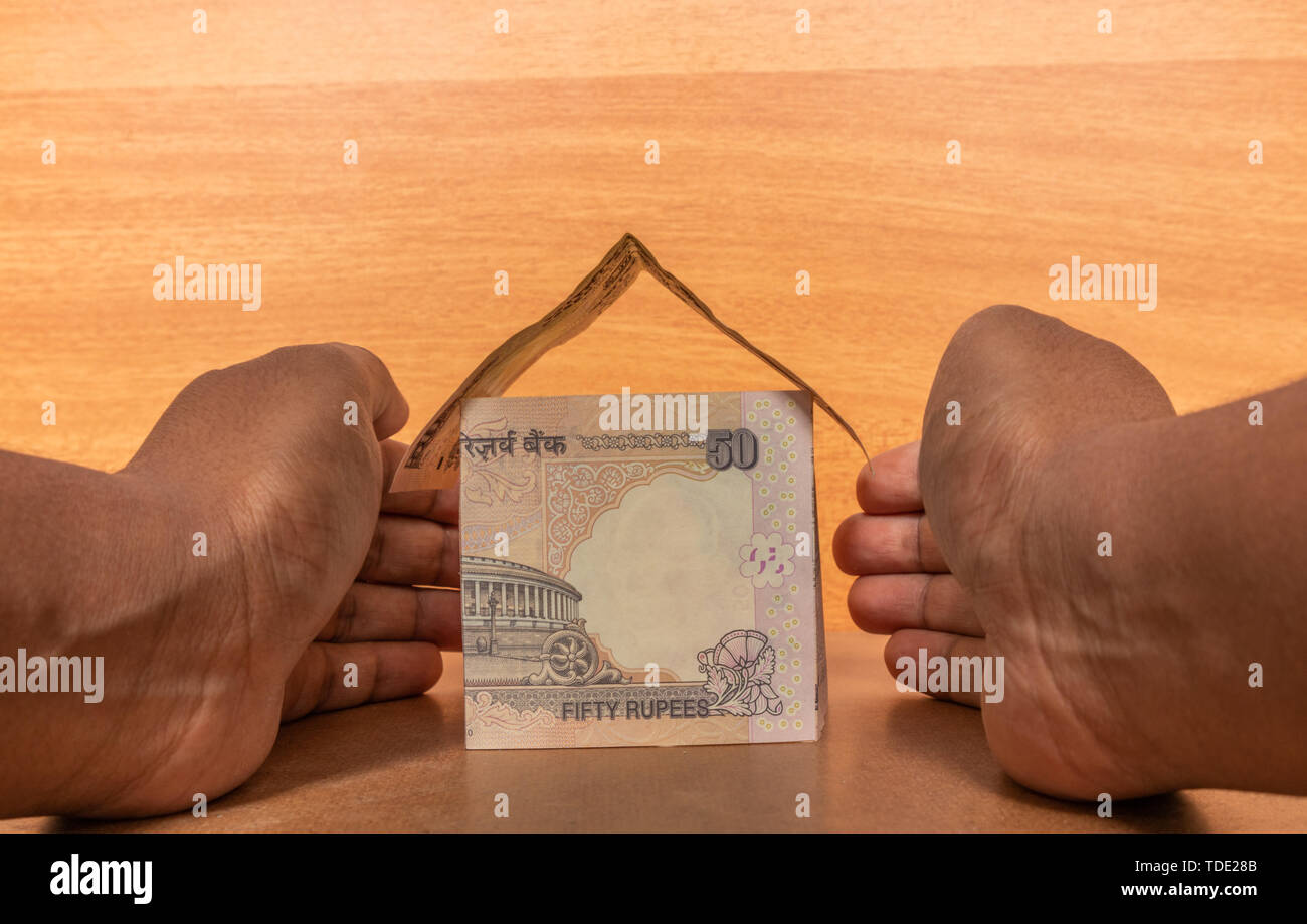 Di proprietà di assicurazione nozione, Mani proteggendo la casa fatta con indiano valuta della carta Foto Stock