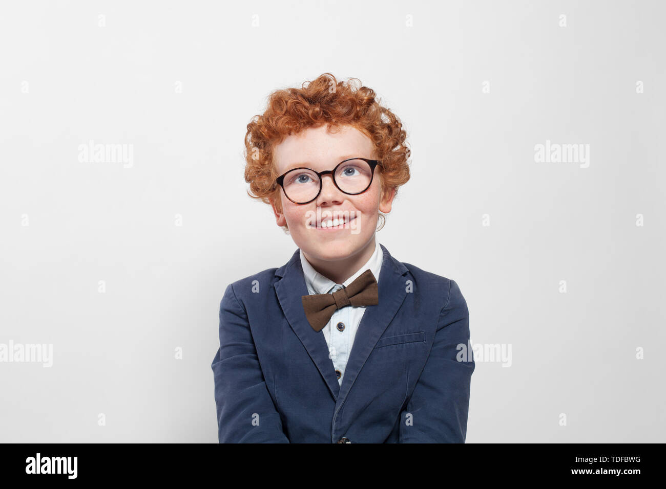 Carino redhead boy in bicchieri cercando su sfondo bianco Foto Stock