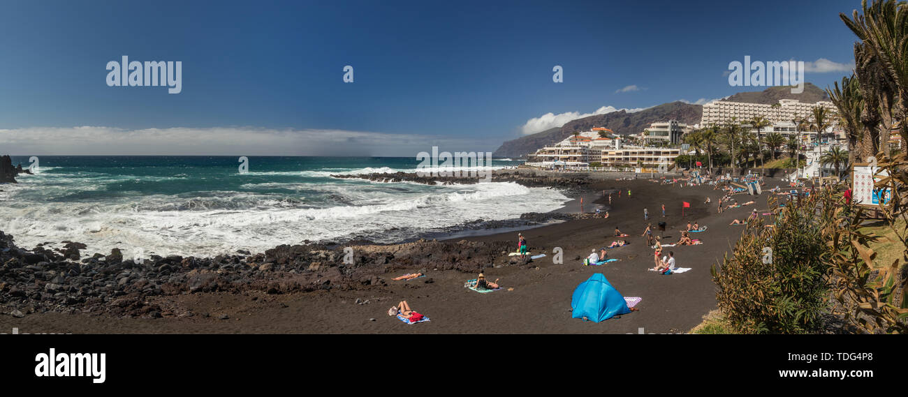 Ripida di lava alte pareti rocciose. Oceano turchese poggia su un luminoso cielo blu e una linea di nuvole sopra l'orizzonte. Playa Arena Beach, Tenerife. Ampia angl Foto Stock