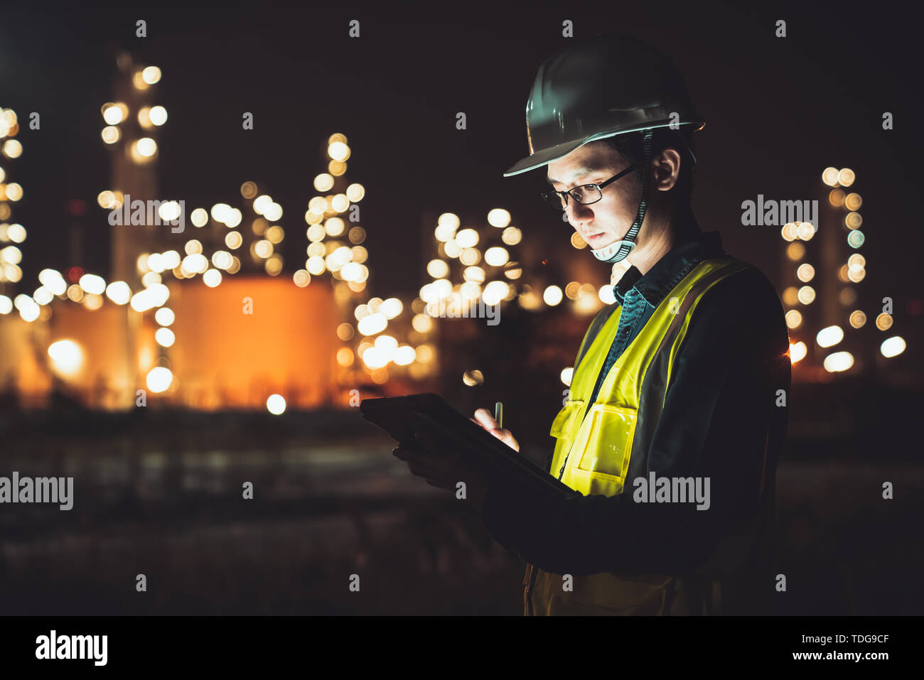Uomo asiatico engineer con tavoletta digitale lavorando fine del turno di notte a olio di petrolio raffineria in industrial estate. Ingegneria chimica, carburante e potenza Foto Stock