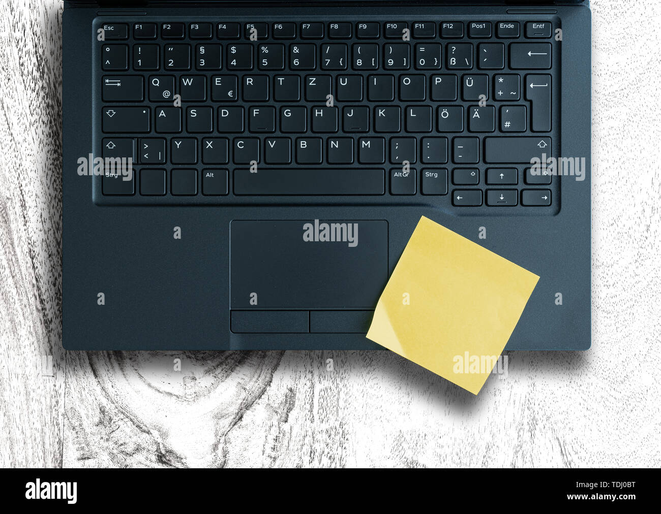 Vista superiore del bigliettino giallo sulla tastiera del laptop bianco contro il tavolo di legno Foto Stock