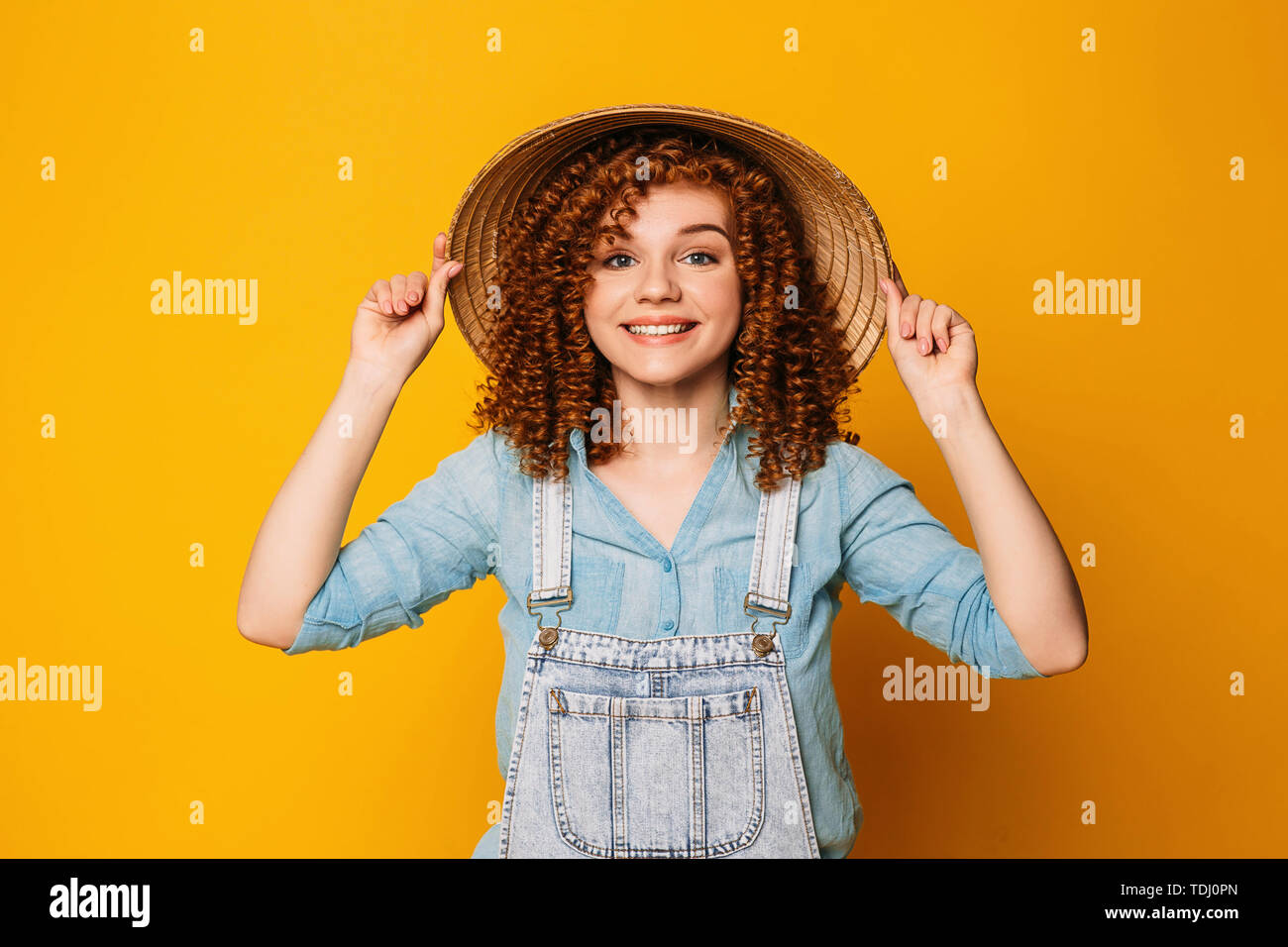 I capelli rossi ricci donna in un cappello di paglia è ridere, su uno sfondo giallo. divertente viaggio, viaggio estivo Foto Stock