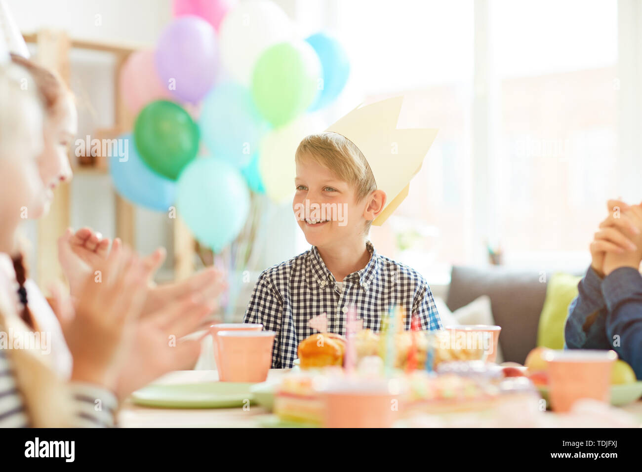 Ritratto di ragazzo sorridente indossando la corona seduta a tavola mentre festeggia il compleanno con gli amici, spazio di copia Foto Stock