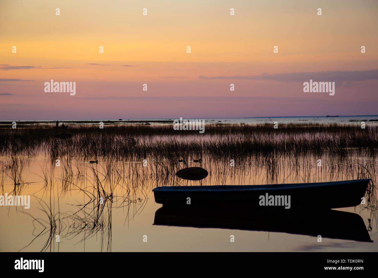 Silhouette di una barca da pesca al di ancoraggio, che si riflette nelle calme e limpide acque del lago, coperto con sedge al tramonto sullo sfondo di una bella multi-colore di Cielo di tramonto. Foto Stock
