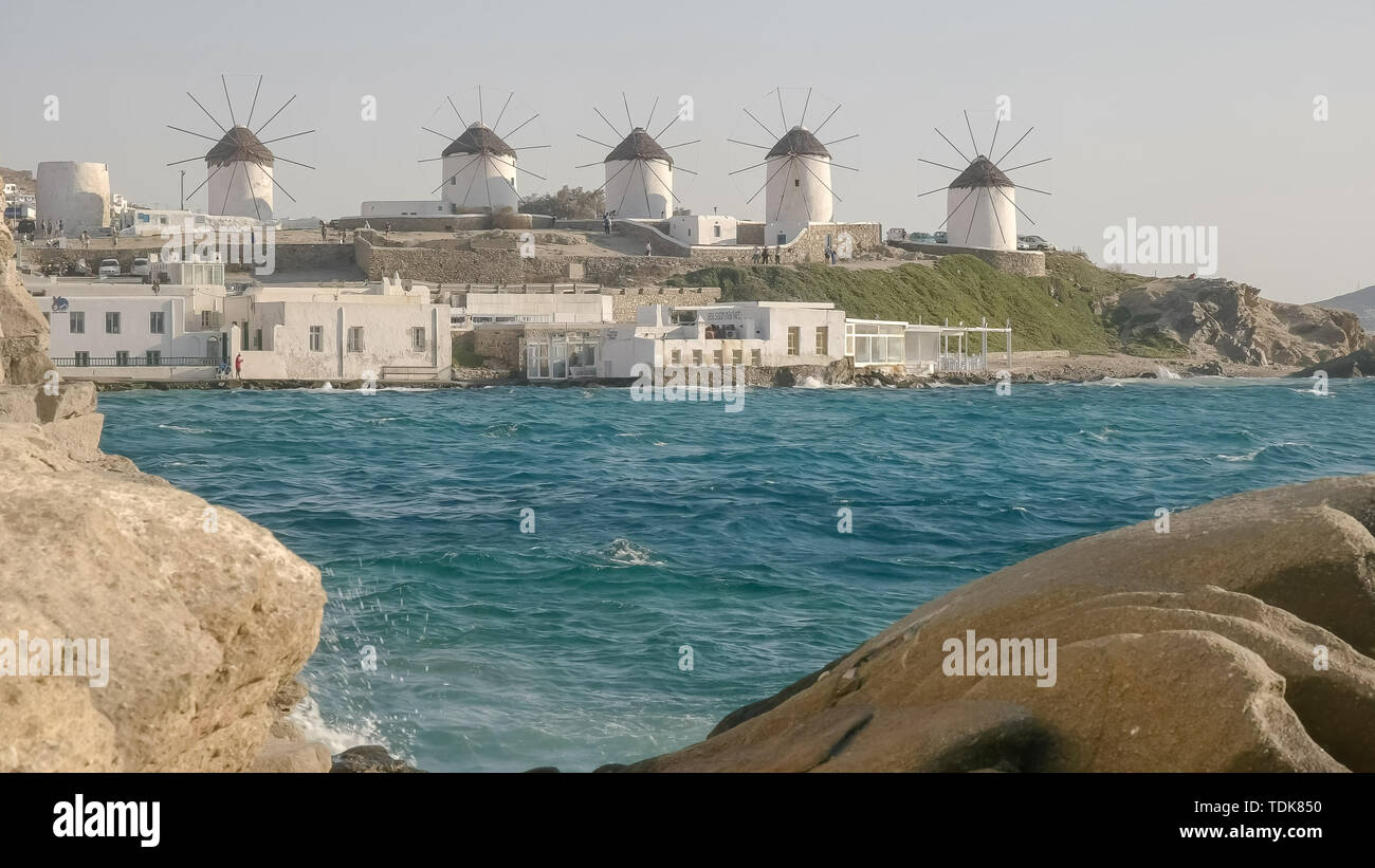 I famosi mulini a vento sull'isola greca di Mykonos incorniciata da una costa rocciosa Foto Stock