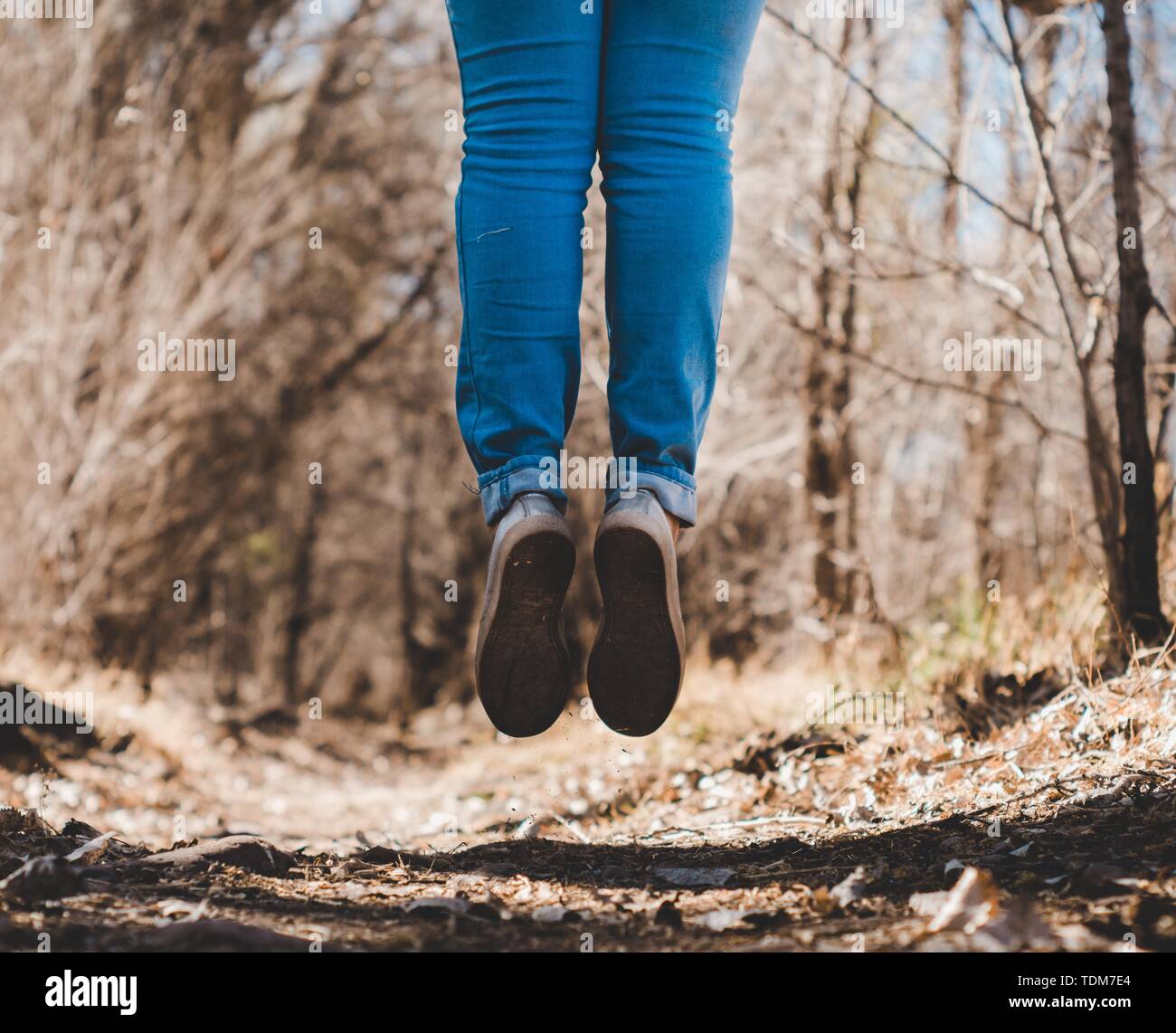 Gambe umane elevate e appese al suolo indossando jeans e scarpe nella foresta Foto Stock