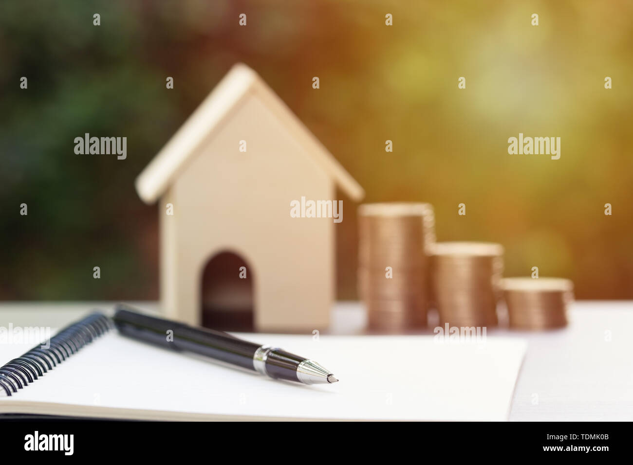 Aziendali e finanziarie il concetto di proprietà per la casa prestito, ipoteca, di risparmio e di investimento. La penna nera sul notebook in bianco con stack sfocata di monete e una Foto Stock