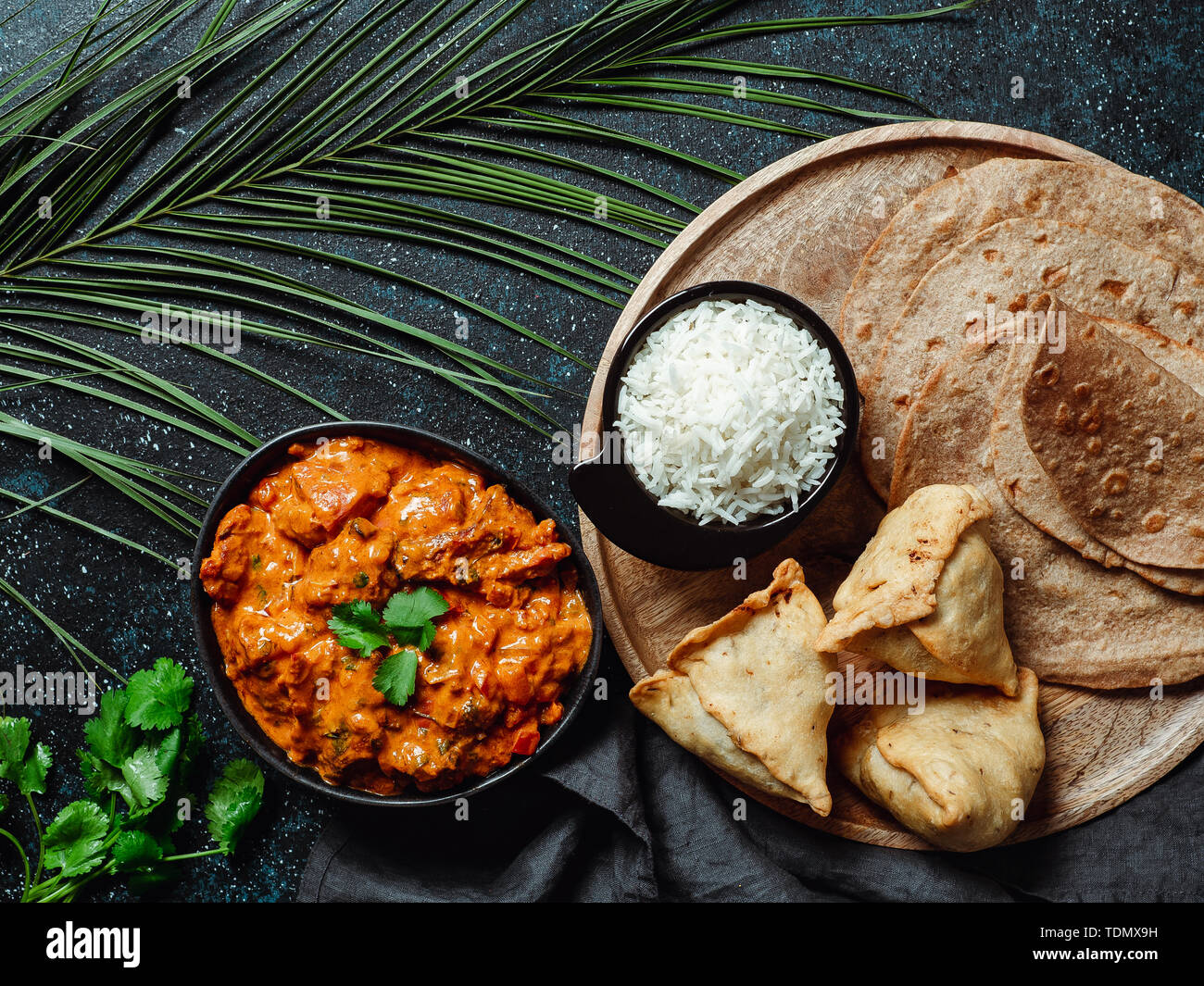 La cucina indiana piatti: tikka masala, riso, samosa, chapati,. Il cibo indiano su sfondo scuro con copia spazio. Assortimento pasto indiano vista superiore piatta o laici. Foto Stock
