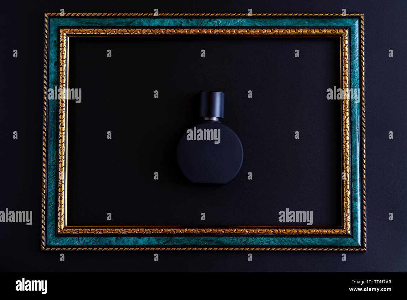 Minimalismo e accessori moda concetto - nero opaco il flacone per profumo unisex close-up all'interno di frame di smeraldo con bordo oro su sfondo scuro Foto Stock