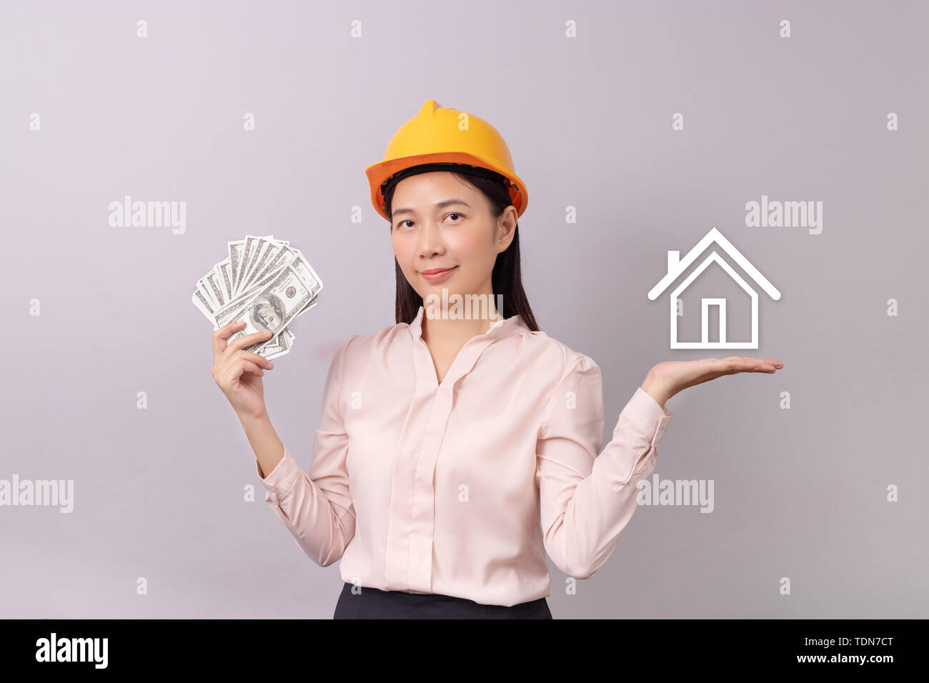 Prestiti per immobili concetto, donna con casco giallo tenendo la banconota soldi in mano e il logo bianco icona home in un altro canto Foto Stock