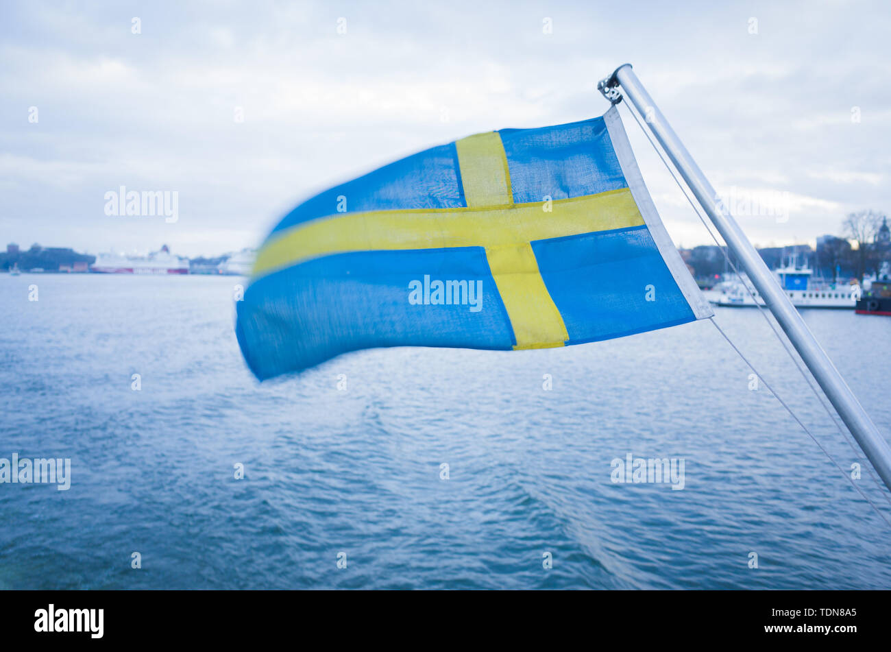 Nazionale svedese sventola bandiera nel vento in poppa di un traghetto navigazione l'arcipelago di Stoccolma su un nuvoloso giornata invernale e. Foto Stock