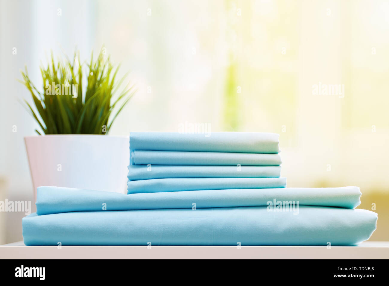 Primo piano della blue lenzuola pulite su uno sfondo sfocato. Una pila di fogli piegati nuove lenzuola sul tavolo. La luce del sole dalla finestra. Foto Stock