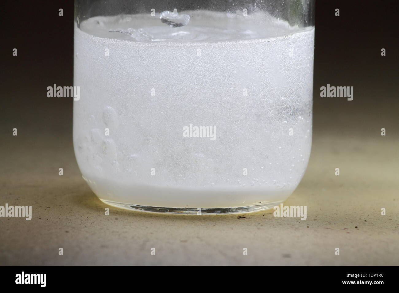 Primo piano di un aceto e bicarbonato di sodio la reazione avvenendo nel fondo di un barattolo di vetro; soluzione torbida Foto Stock