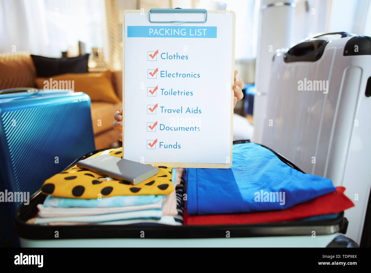 Primo piano sul giovane viaggiatore donna in blu t-shirt a casa moderna nella soleggiata giornata estiva che mostra lista di imballaggio. Foto Stock
