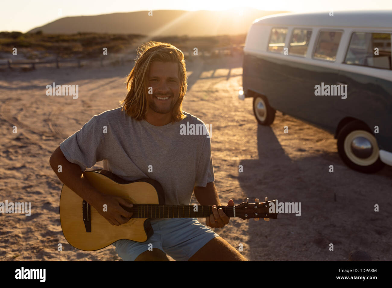 Felice giovane a suonare la chitarra nei pressi di camper presso la spiaggia Foto Stock