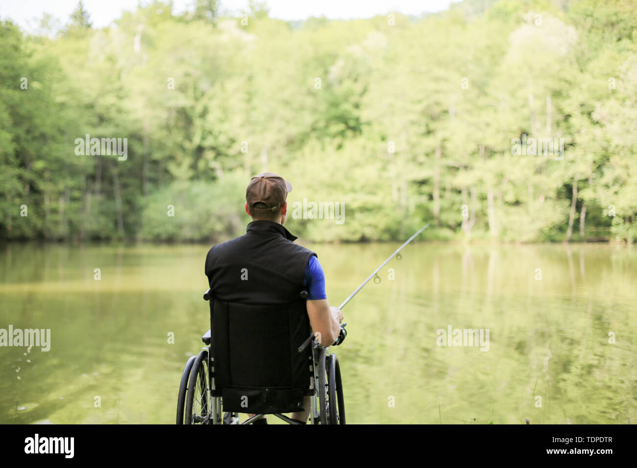 Felice e giovani disabili o handicappati uomo pesca in un lago in natura. Sport popolari per paraplegici. Foto Stock