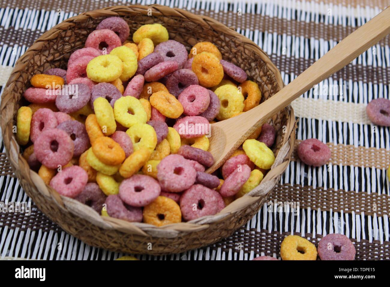 Piccolo vaso in vimini con colorati round cereali e cucchiaio di legno Foto Stock