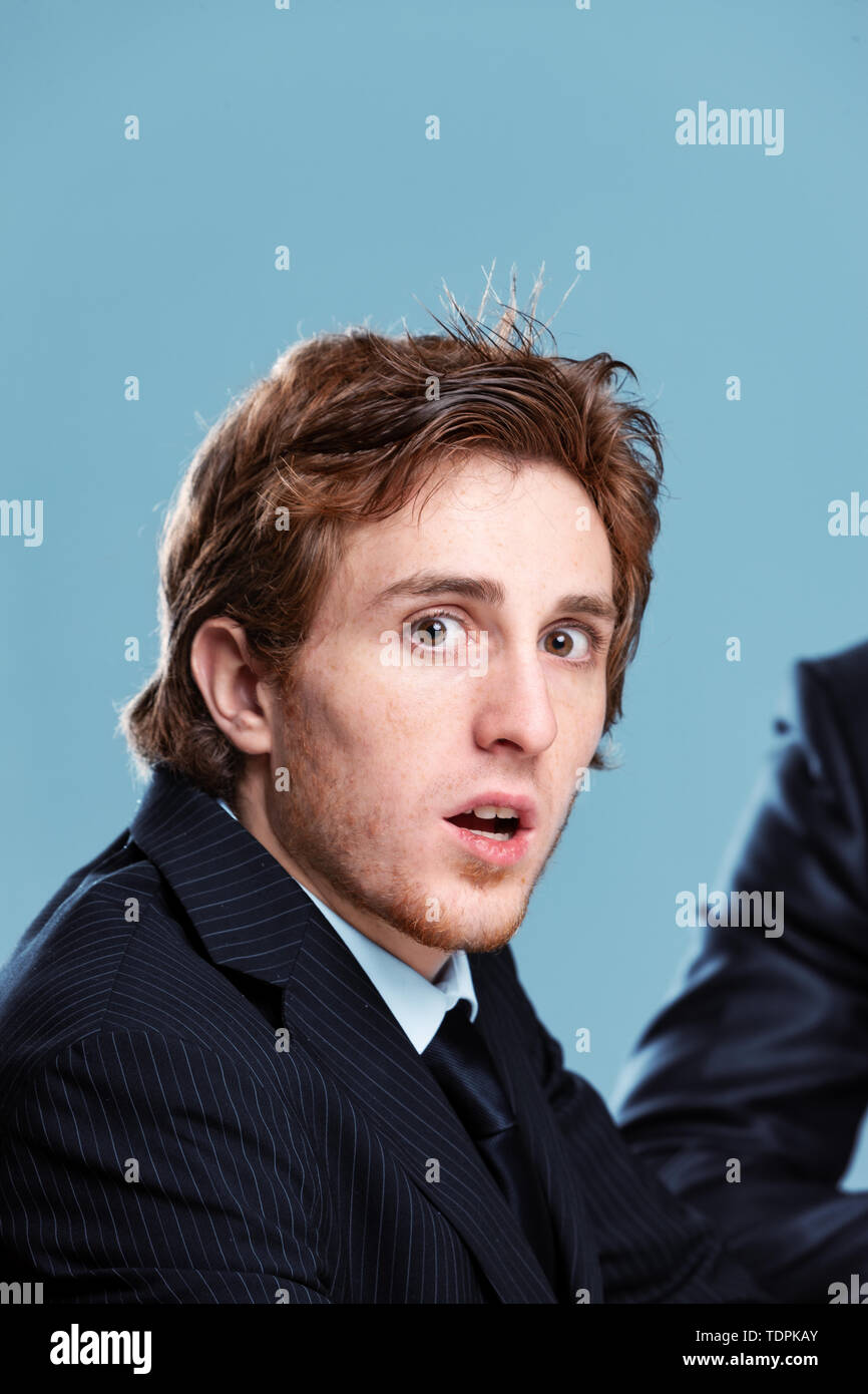 Scioccato imprenditore girando a gawp presso la fotocamera con la bocca aperta e occhi spalancati come egli si siede in un incontro con un collega o un boss Foto Stock