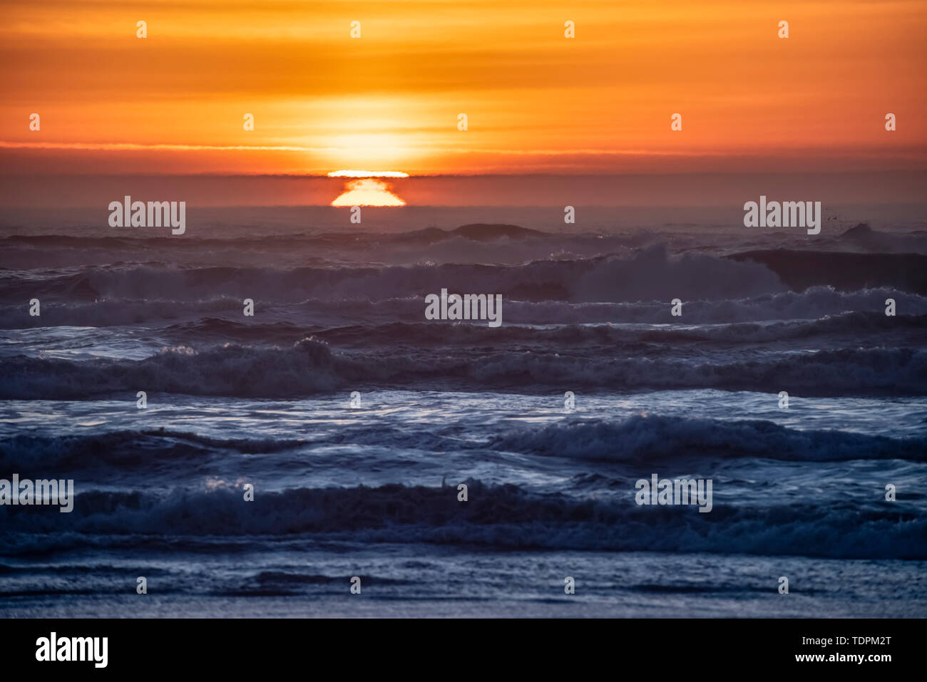 Tramonto sulle onde a Cape Disappointment, Washington. L'inversione atmosferica fa sì che il sole appaia in più posizioni contemporaneamente. Questo i... Foto Stock