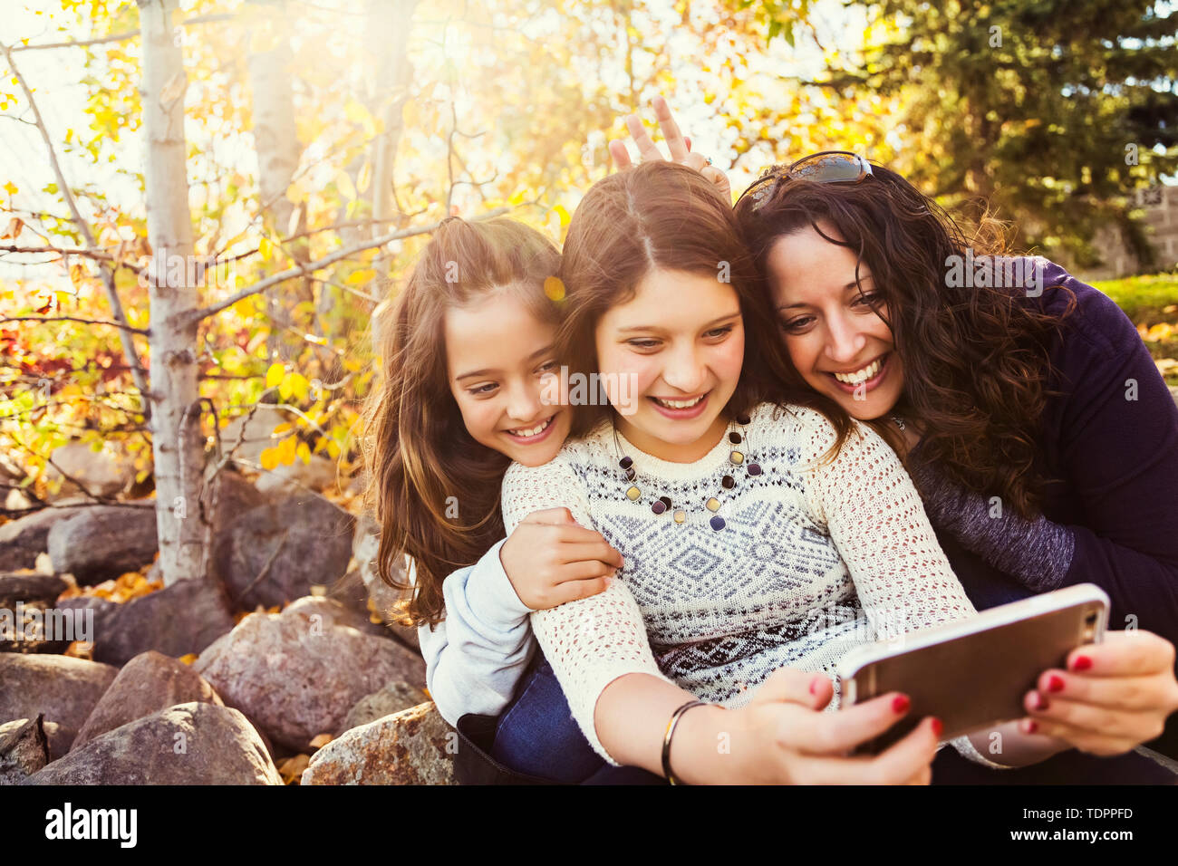 Una mamma e le sue due figlie prendendo un autoritratto durante il riposo durante una gita di famiglia in un parco della città in una calda giornata di caduta; Edmonton, Alberta, Canada Foto Stock