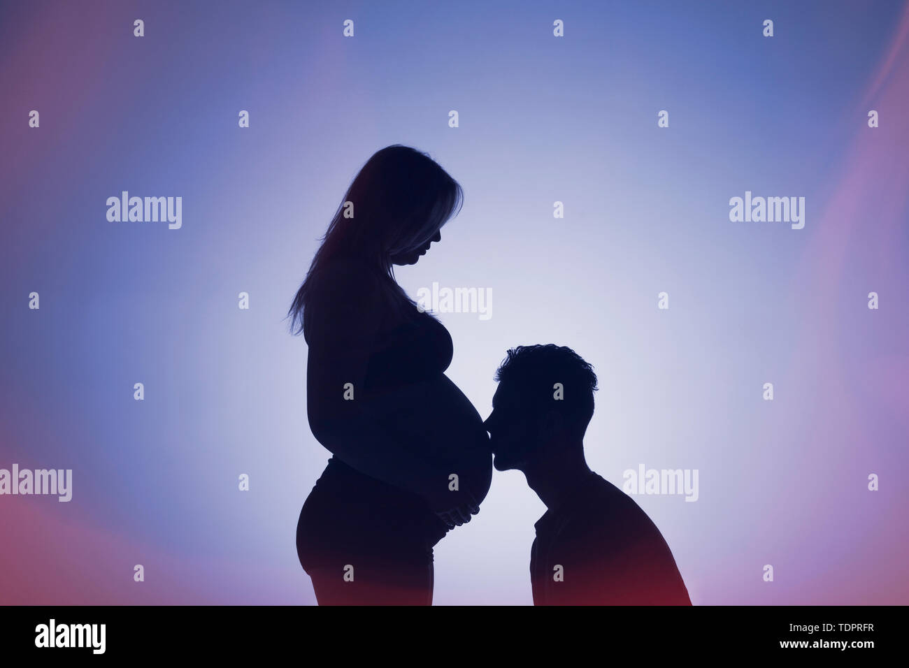 Una silhouette in uno studio di un giovane che stanno avendo un bambino e il padre sta baciando la madre della pancia che è ben lungo nel suo stato di gravidanza Foto Stock