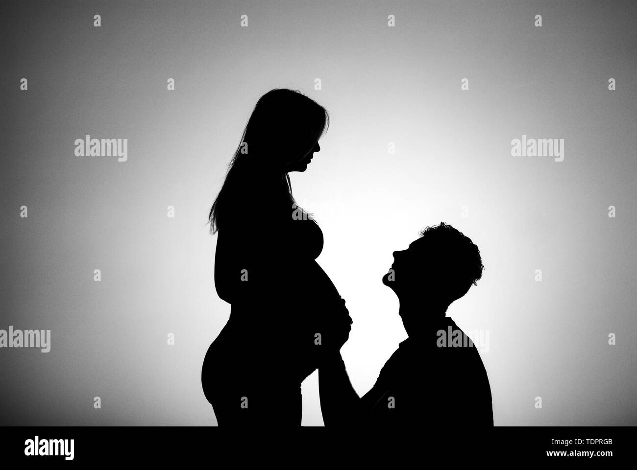 Una silhouette in uno studio di un giovane che stanno avendo un bambino e il padre è toccante della madre e del ventre che è ben lungo nel suo stato di gravidanza Foto Stock