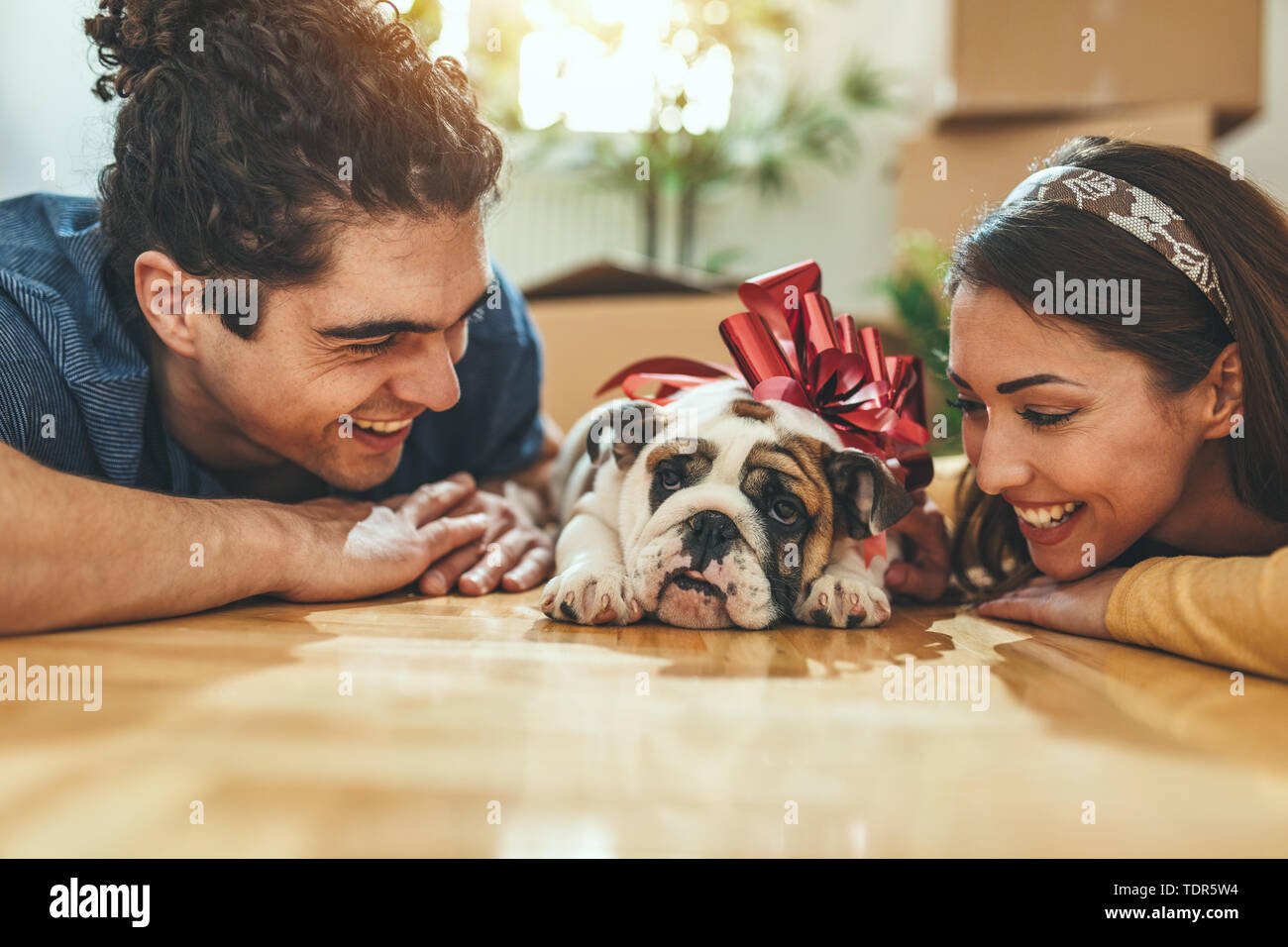 La giovane coppia felice si trasferisce in una nuova casa. Sono sdraiato sul pavimento con il loro piccolo cucciolo dopo che avevano portato a caselle con cose da th Foto Stock