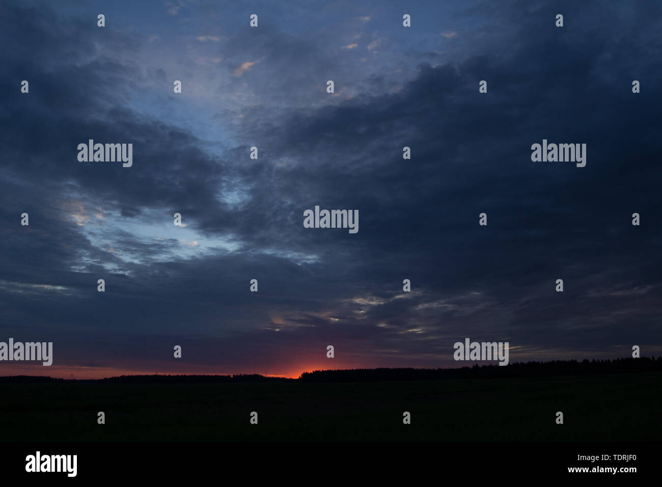 Masterizzazione luminosamente il tramonto in un campo con le nuvole grigio Foto Stock