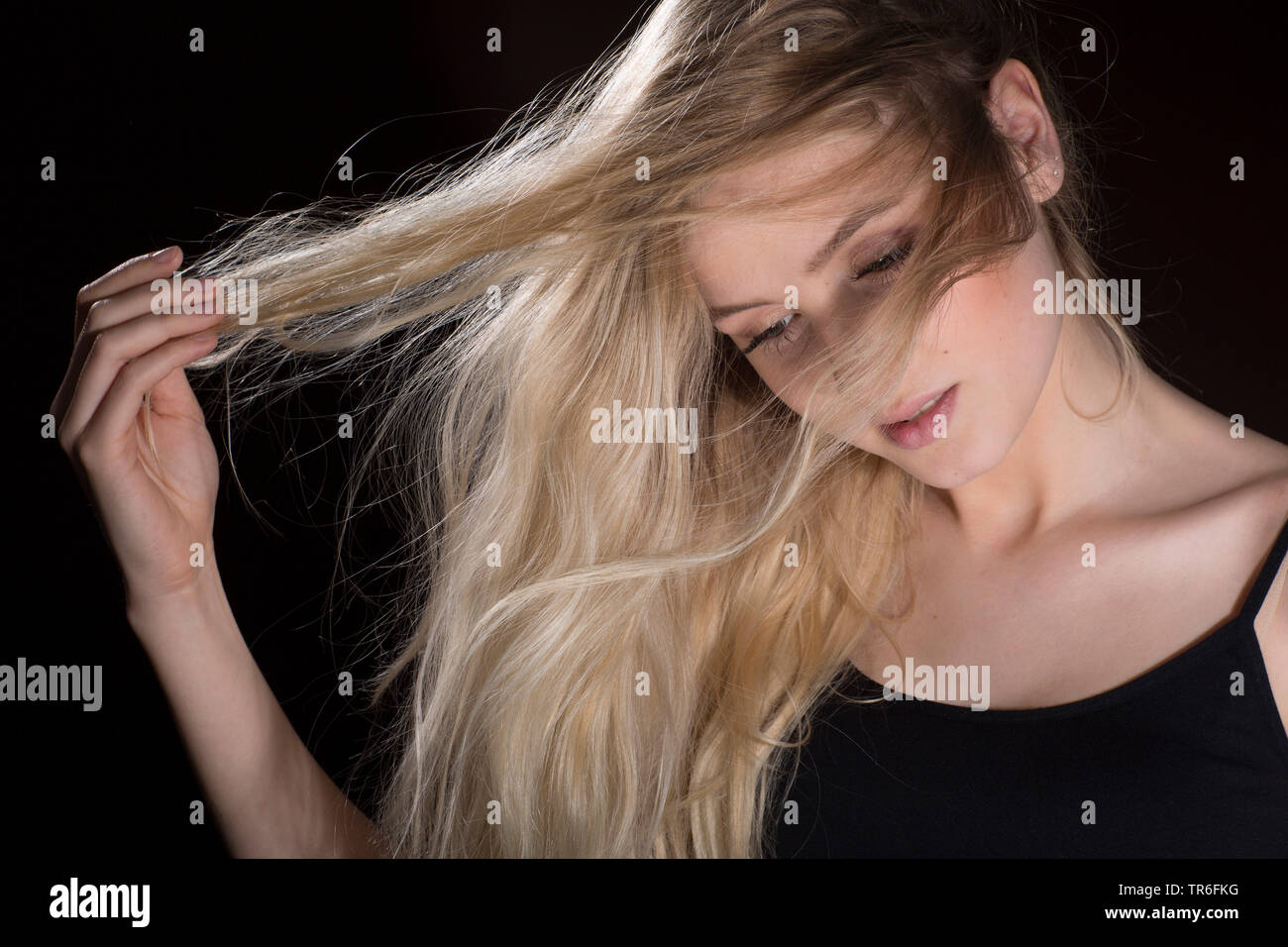 Giovane donna bionda, perso nel pensiero, eseguono le dita attraverso i suoi capelli, Germania Foto Stock